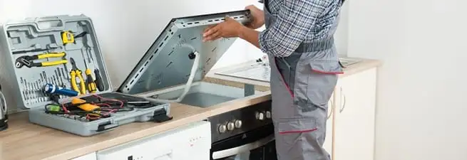 Cooktop repair technician lifting a built-in stovetop for service in Pasadena, CA