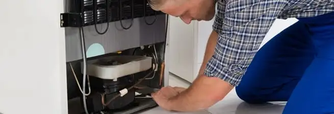 Refrigerator repair technician servicing the compressor and condenser area in Pasadena, CA