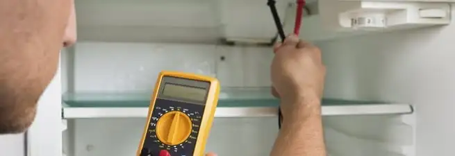 Refrigerator repair technician testing electrical components with a multimeter in Pasadena, CA